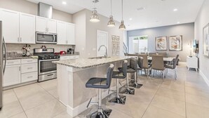 A modern kitchen with white cabinets, stainless steel appliances, and a central island with bar stools. - Sunrise Shores 4 Bedroom Townhouse (Kissimmee)