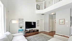 A spacious living room with a large flat-screen TV, a white sofa, a blue side table, and a patterned rug. - Endless Summer 6 Bedroom Home (Kissimmee)
