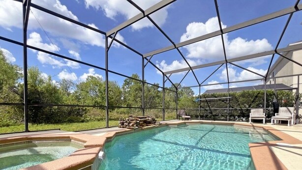 A swimming pool with a metal safety fence, surrounded by a landscaped area with trees and a building in the background. - Willow View 4 Bedroom Home (Davenport)