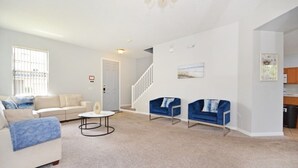 A spacious living room with a white sofa, a blue sofa, and a coffee table. There is a staircase leading to another level. - Willow View 4 Bedroom Home (Davenport)