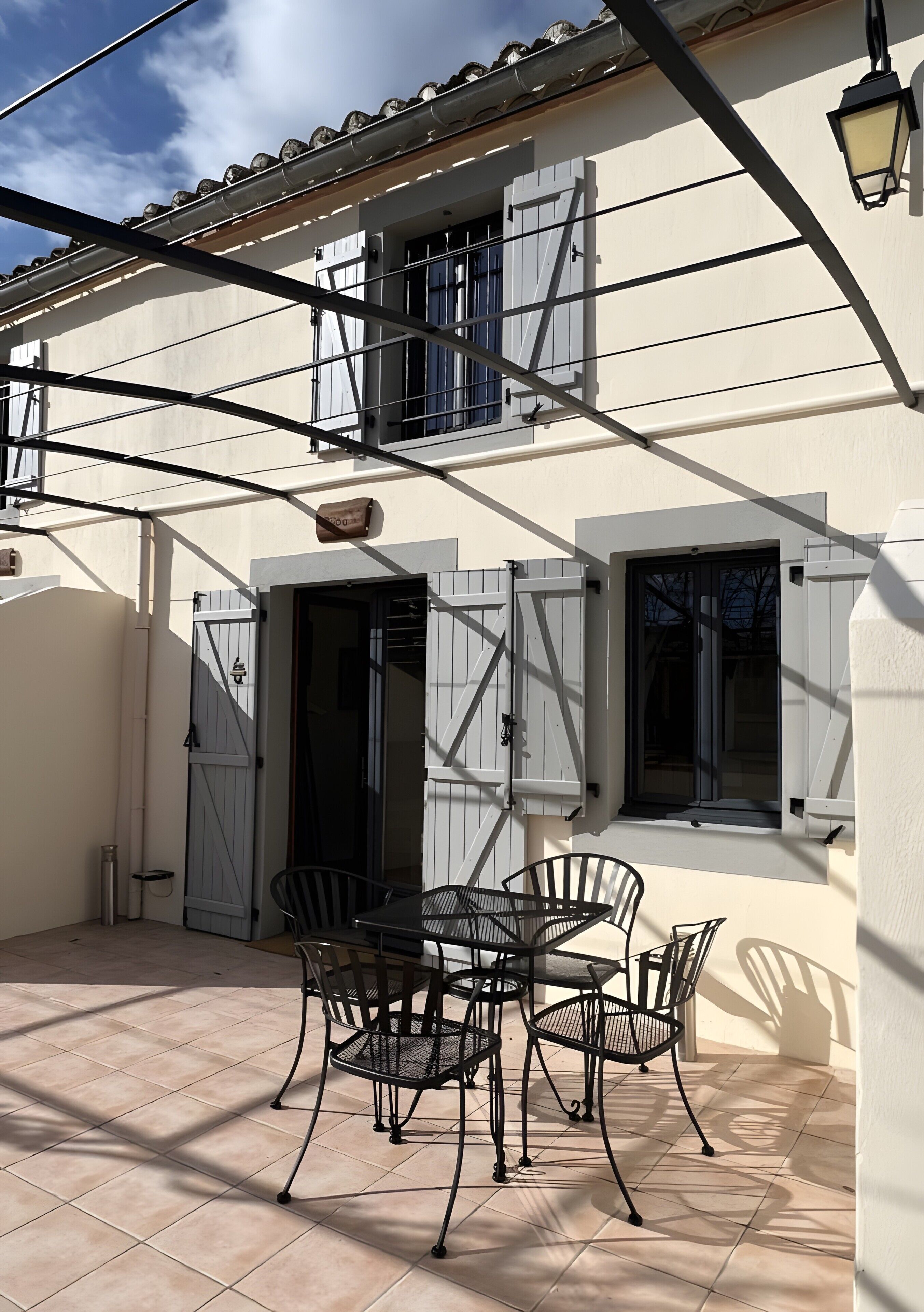 Eine Terrasse mit Tisch und Stühlen, ein Tor und ein Gebäude mit Fensterläden und einem Fenster.