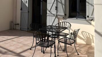 Eine Terrasse mit Tisch und Stühlen, ein Tor und ein Gebäude mit Fensterläden und einem Fenster.