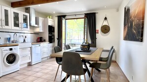 Una cocina moderna con electrodomésticos integrados, un comedor con mesa y sillas, y un amplio ventanal con cortinas.