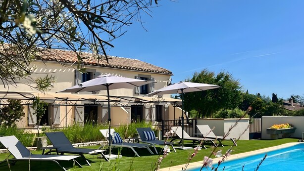Un área junto a la piscina con sillones de descanso, sombrillas y una piscina.