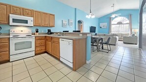 Eine moderne Küche mit Holzausstattung, Mikrowelle, Herd und Geschirrspüler. Es gibt einen Essbereich mit Tisch und Stühlen sowie ein Wohnzimmer mit Sofa und Fernseher.