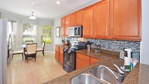 A kitchen with wooden cabinets, a stainless steel sink, a microwave, and a dining area with chairs and a table. - Ohana Haven 5 Bedroom Home (Kissimmee)