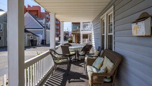 A covered porch with wicker furniture and a table, overlooking a street with other buildings. - Mallard 2A close to the Beach (Ocean City)