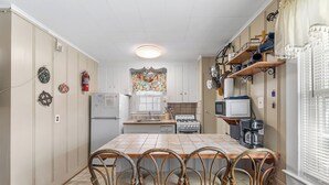 Keittiössä on laatoitettu keittiösaareke, puiset tuolit, jääkaappi, liesi, mikroaaltouuni ja kahvinkeitin.