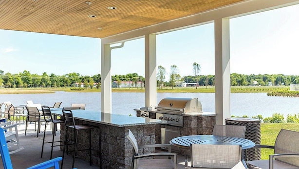 An outdoor patio with a stone bar, grill, and seating area overlooking a lake. - Belle Beach Retreat at Millville by the Sea (Millville)