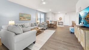 A living room with a sofa, coffee table, and TV stand. There is a dining area with a table and chairs. - Belle Beach Retreat at Millville by the Sea (Millville)