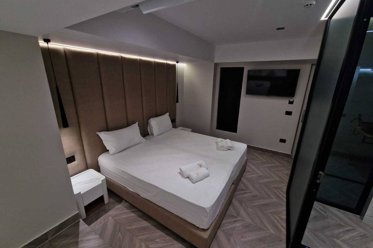 Habitació d'hotel moderna amb un llit gran, una tauleta de nit i un televisor penjat a la paret.