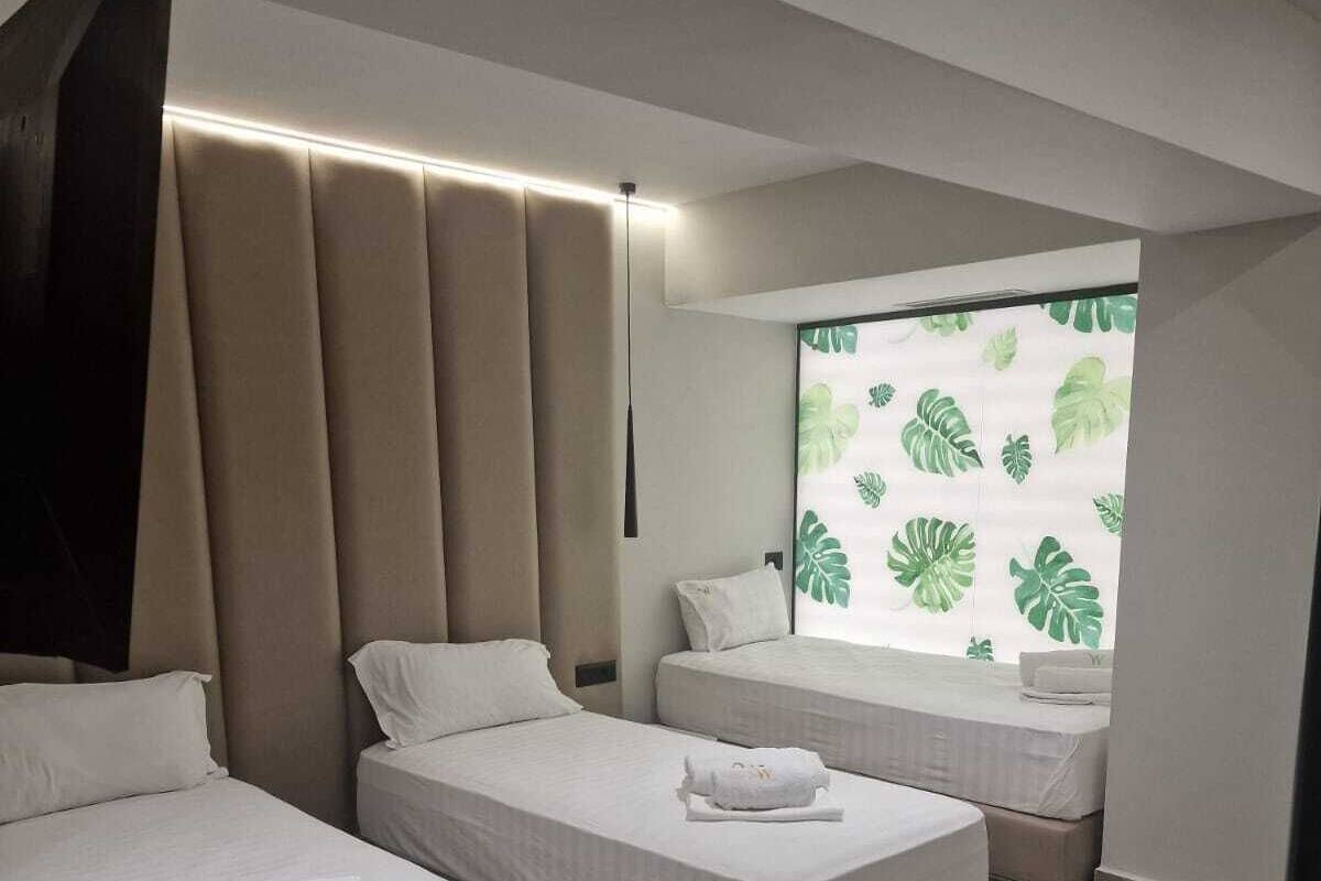 Habitació d'hotel amb dos llits, una finestra gran amb un dibuix de plantes i un disseny modern.