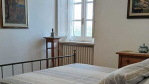 Quarto com cama, janela, radiador, mesa de cabeceira e duas molduras na parede.