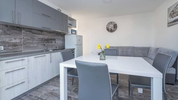 Una cocina moderna con armarios grises, una encimera blanca y una zona de comedor con una mesa blanca y sillas grises.
