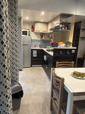Eine moderne Küche mit Kühlschrank, Mikrowelle und Gasherd. Ein Spülbecken mit Wasserhahn ist vorhanden, und ein Mülleimer ist sichtbar.