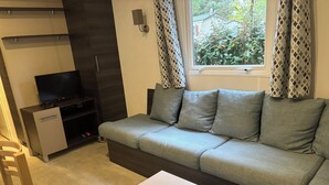 Moderni olohuone, jossa on harmaa sohva, litteänäyttöinen televisio, pieni kaappi ja ikkuna, jossa on kuviolliset verhot.