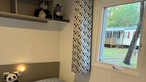 Huoneessa on kaksi sänkyä, hylly täytetty pehmoleluilla, ikkuna, josta avautuu näkymä puuhun ja rakennukseen, sekä geometrisesti kuvioitu verho.