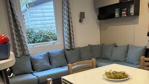 Moderni olohuone, jossa on harmaa sohva, ruokapöytä tuoleineen ja ikkuna, jossa on kuviolliset verhot.