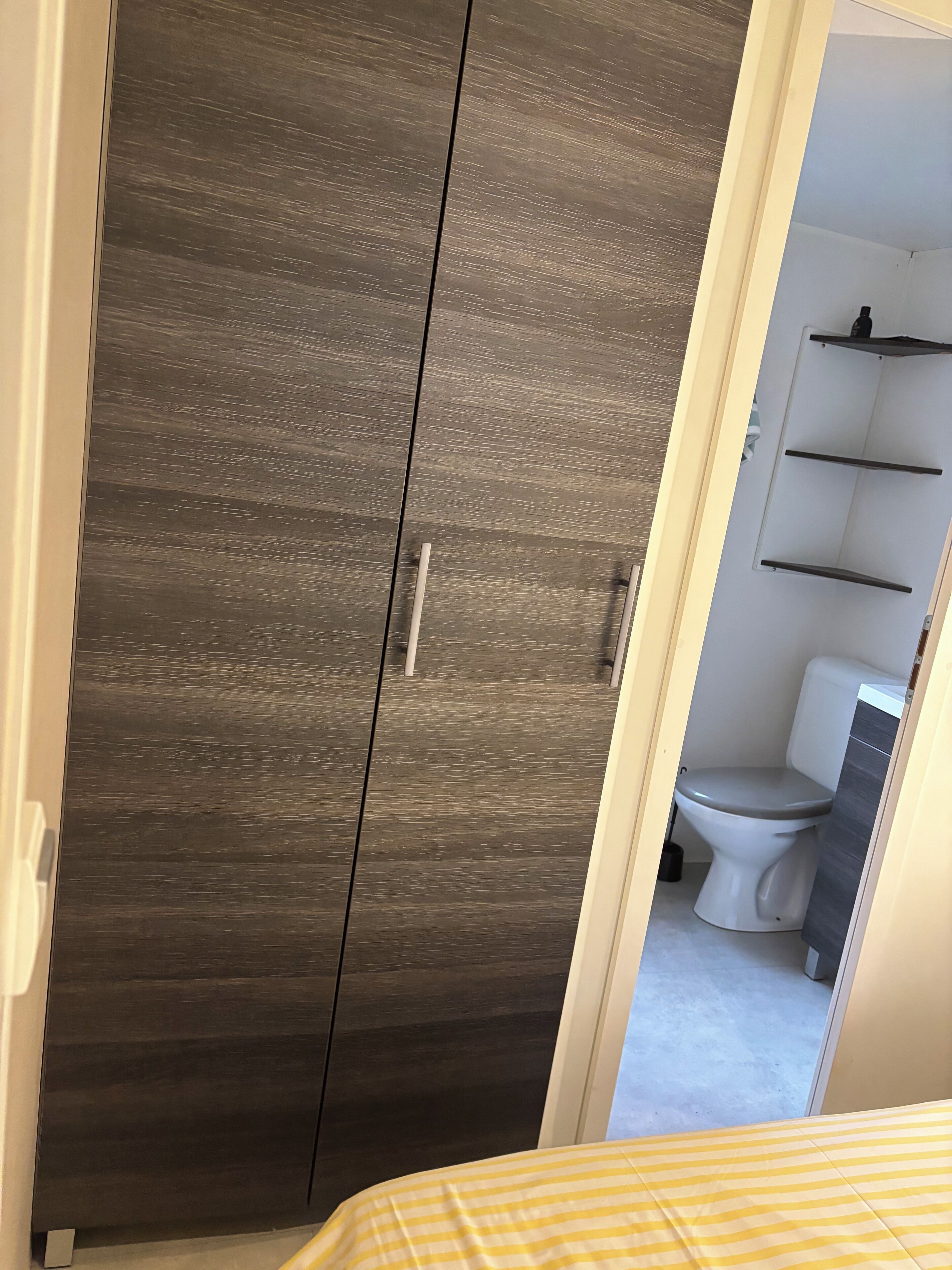 Un dormitorio con cama, armario y baño visible a través de una puerta abierta.