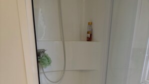 Lasiseinöillä varustettu suihku, jossa on valkoinen lattia, vihreä-valkoinen raidallinen matto ja shampoopullo hyllyllä.
