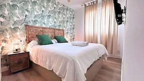 A neatly made bed with white linens and green pillows, a wooden nightstand with a lamp, and a wall with a leafy pattern. - Balcony of the Sea (El Morche)