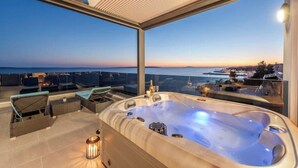 En tagterrasse med jacuzzi, siddeområde og havudsigt i solnedgangen.