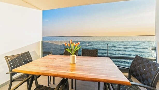 A wooden table with four chairs and a vase of flowers on a balcony with a view of the sea. - Blue waves apartment (Mandre)