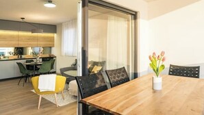 A modern dining area with a wooden table, black chairs, and a yellow chair. There is a vase with flowers on the table. - Blue waves apartment (Mandre)
