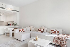 A modern living room with a white sectional sofa, a small coffee table, and a kitchen area in the background. - 2BR M Room CF7 B Near Jumeirah Beaches (Dubai)