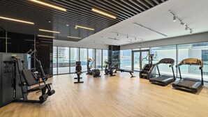 A modern gym with various exercise equipment, large windows, and a wooden floor. - 2BR M Room CF7 B Near Jumeirah Beaches (Dubai)