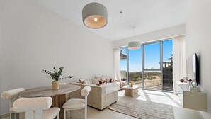 A modern living room with a sofa, dining table, and chairs. There is a large window with a view of the city. - 2BR M Room CF7 B Near Jumeirah Beaches (Dubai)