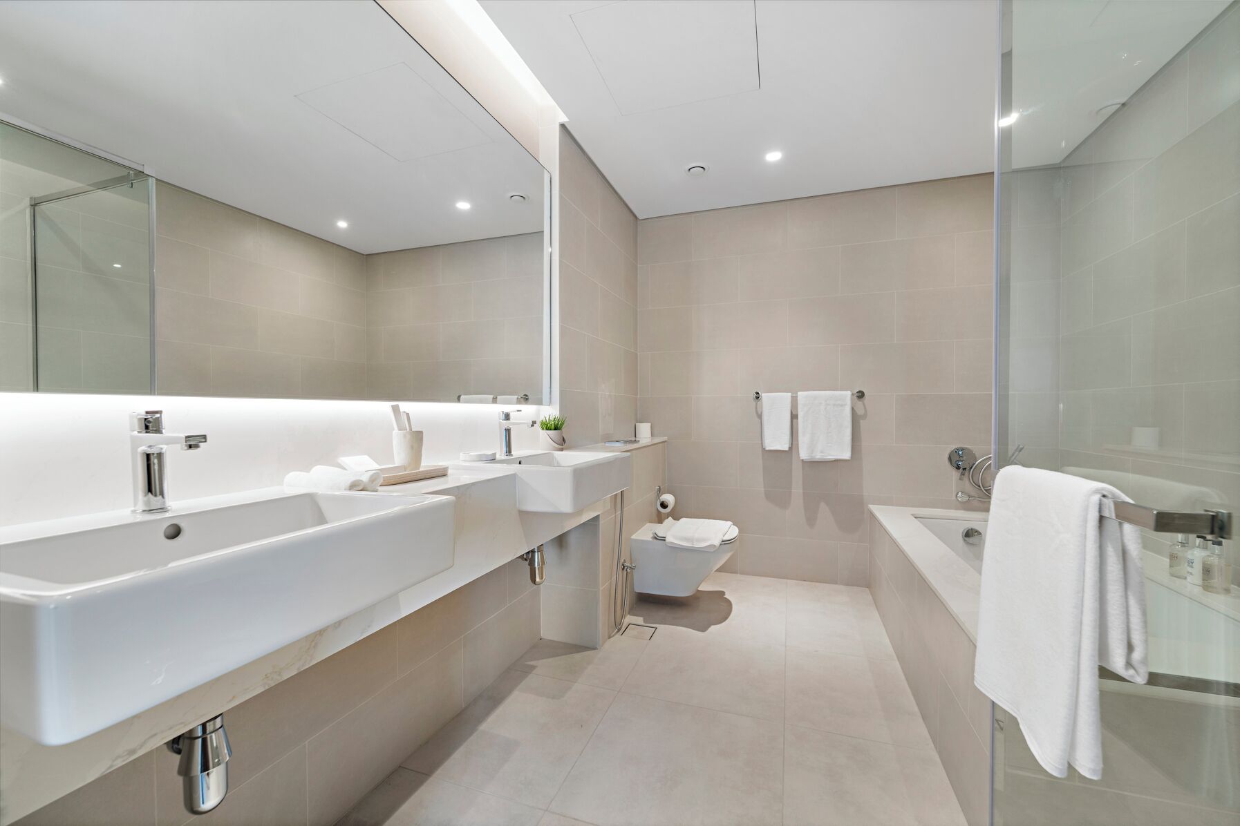 A modern bathroom with a large mirror, a bathtub, a toilet, and a shower area.