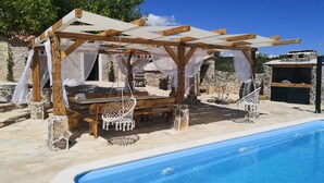 A poolside area with a wooden pergola, white canopy, and a hanging chair. - Juniper Stone Cottage by Villas Guide (Benkovac)