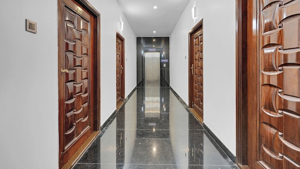 A hallway with wooden doors and a polished black floor. - Olive Lakeview Serviced Apartments (Chennai)