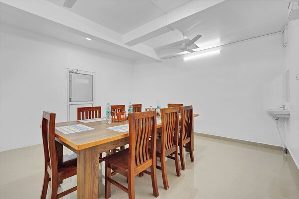 Uma sala de conferências com mesa de madeira, seis cadeiras, um quadro branco e um ventilador de teto.
