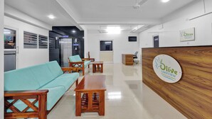 A reception area with a wooden reception desk, a blue sofa, and a wooden coffee table. - Olive Lakeview Serviced Apartments (Chennai)