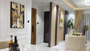 A modern living room with a marble island, beige armchairs, and a large abstract painting on the wall. - Luxury 3 bedrooms in a secured and serene environment 10mins to the Int Airport (Ikeja)