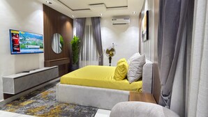 A modern bedroom with a bed, a TV, an air conditioner, and a sofa. - Luxury 3 bedrooms in a secured and serene environment 10mins to the Int Airport (Ikeja)