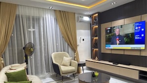 A modern living room with a sofa, armchair, coffee table, and a flat-screen TV mounted on the wall. - Luxury 3 bedrooms in a secured and serene environment 10mins to the Int Airport (Ikeja)