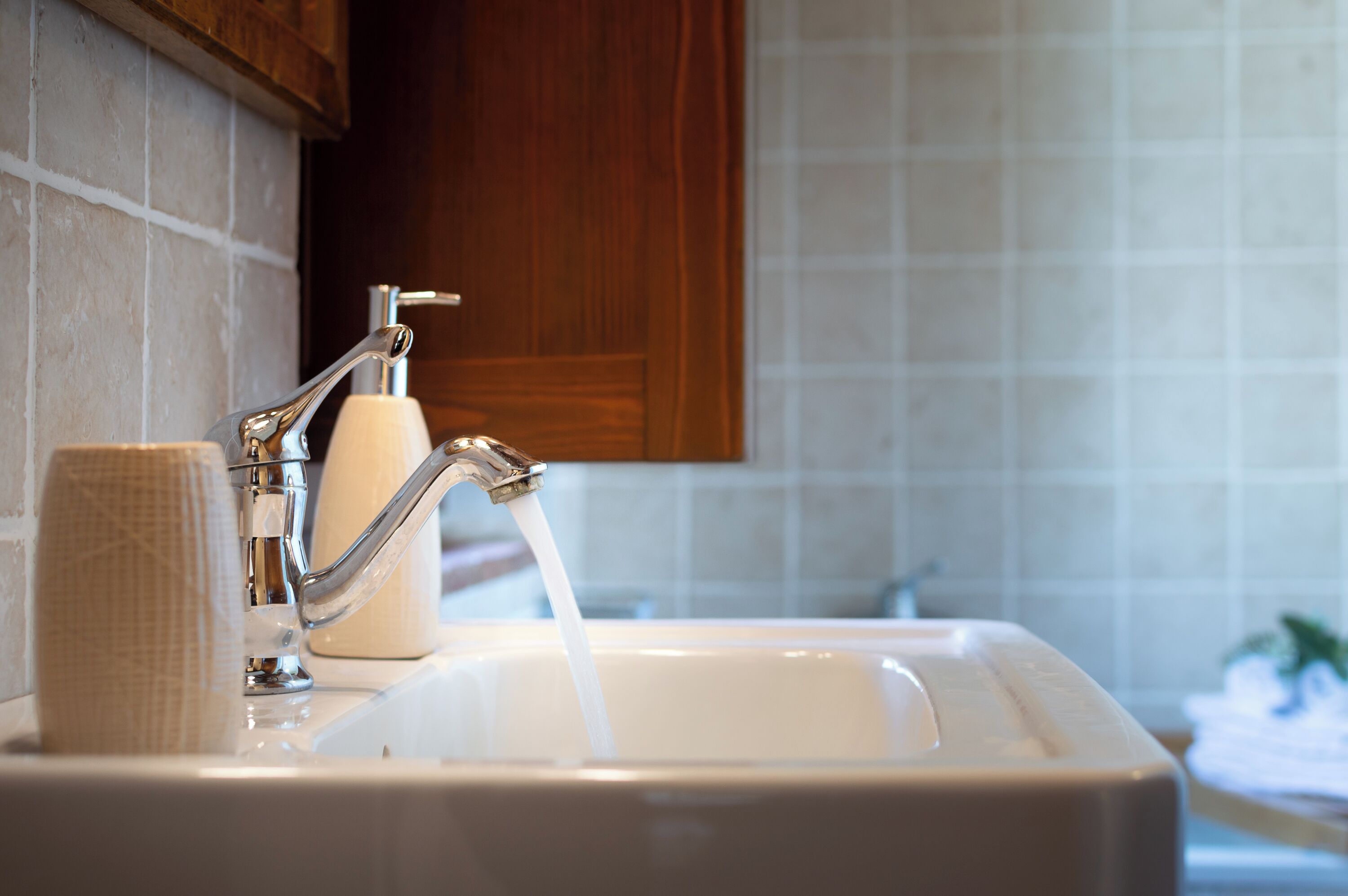 Un lavabo con rubinetto aperto, un erogatore di sapone e un asciugamano.