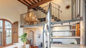 A spacious living area with a loft bedroom, a staircase, and a rustic brick fireplace. - Apartment la Torre, Palazzo Monaci - with Swimming Pool in the Crete Senesi (Toscana)
