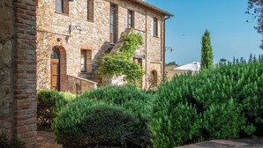 A stone building with a brick facade, a staircase, and a garden with green shrubs. - Apartment la Torre, Palazzo Monaci - with Swimming Pool in the Crete Senesi (Toscana)