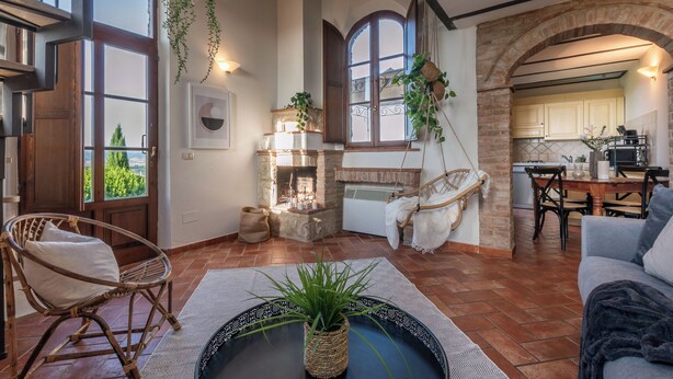 A cozy living room with a fireplace, a dining area, and a kitchen visible through an archway. - Apartment la Torre, Palazzo Monaci - with Swimming Pool in the Crete Senesi (Toscana)