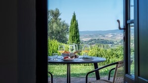A table set with plates, glasses, and a bowl of food, overlooking a lush garden and distant hills. - Apartment la Torre, Palazzo Monaci - with Swimming Pool in the Crete Senesi (Toscana)