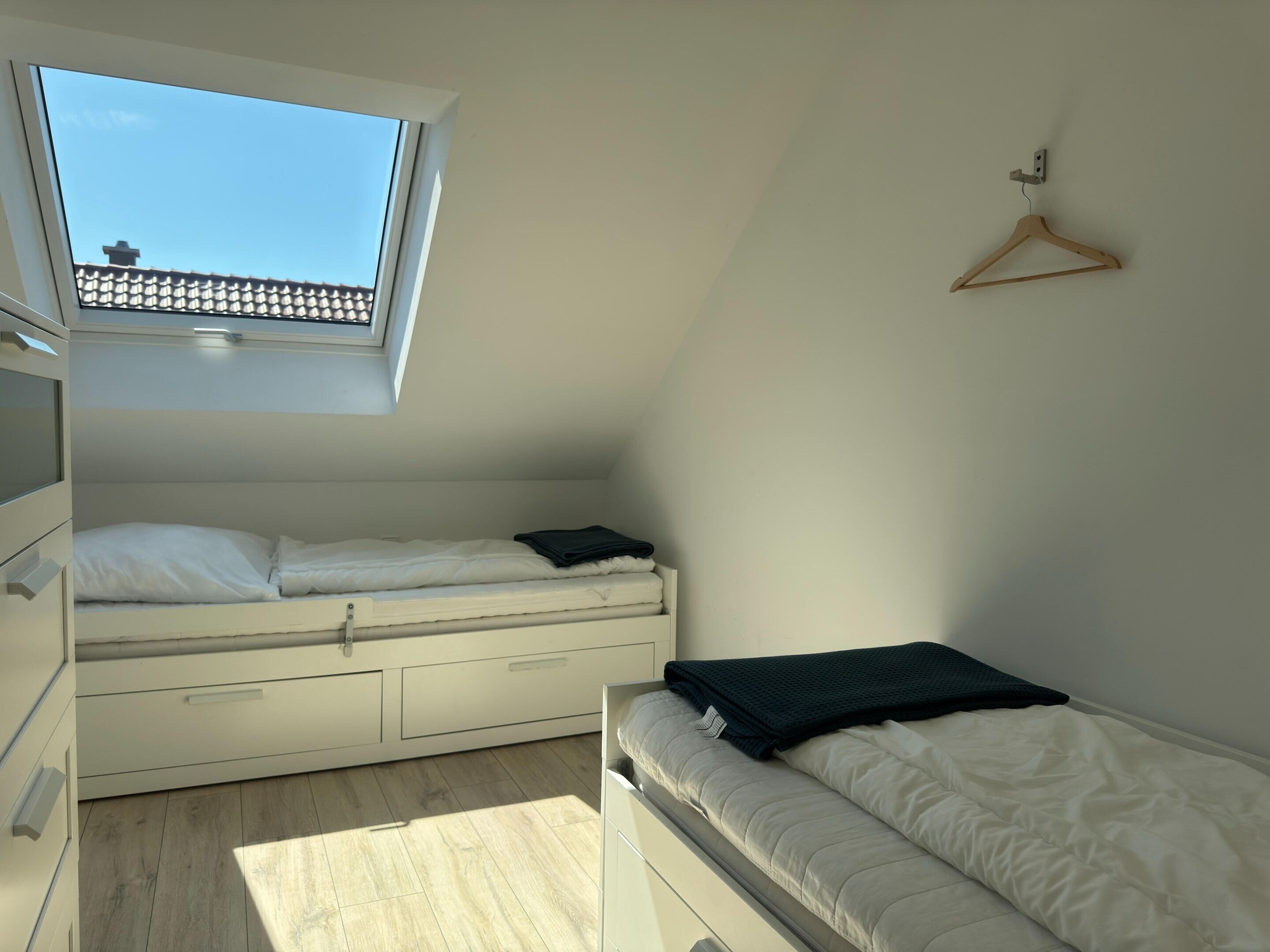A bedroom with a skylight, two beds, a wooden hanger, and a white wardrobe.