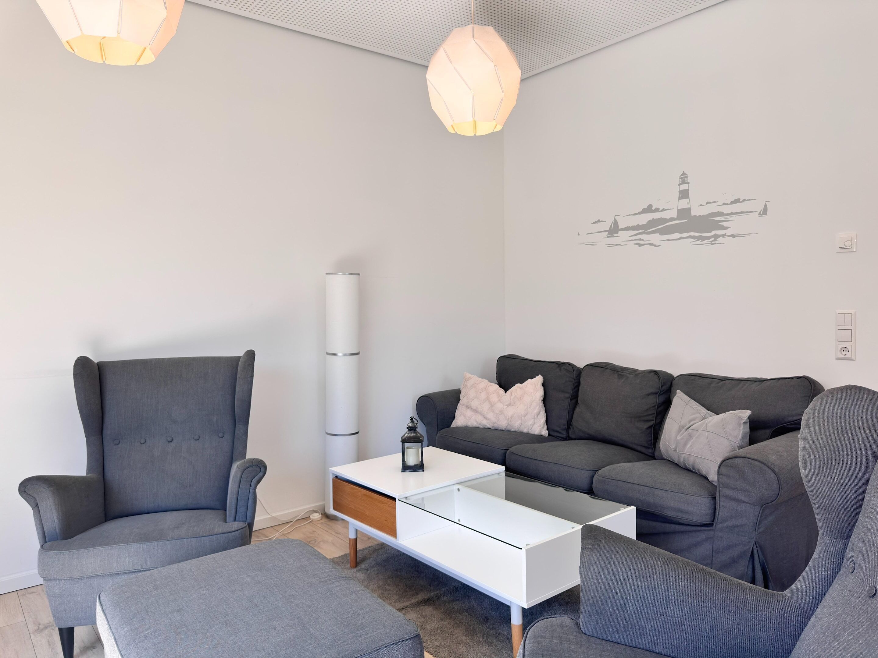 A modern living room with a grey sofa, a white coffee table, and a grey armchair.