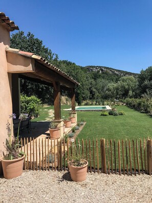 Ein überdachter Patio-Bereich mit Pool, umgeben von einem gepflegten Rasen und einem Holzzaun.