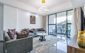 Una sala moderna con un sofá gris, una mesa de centro redonda y un amplio ventanal con vistas al exterior.