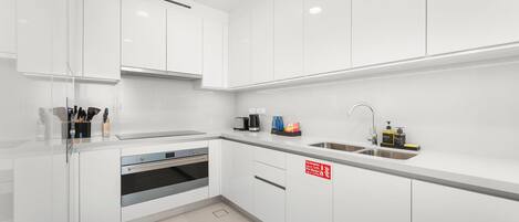 A modern kitchen with white cabinets, a stainless steel sink, and a built-in oven.