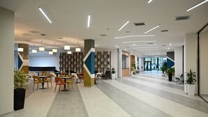 A modern office space with a long reception area, multiple seating arrangements, and a large bookshelf. - Arena Hotel Yevlakh (Yevlakh)